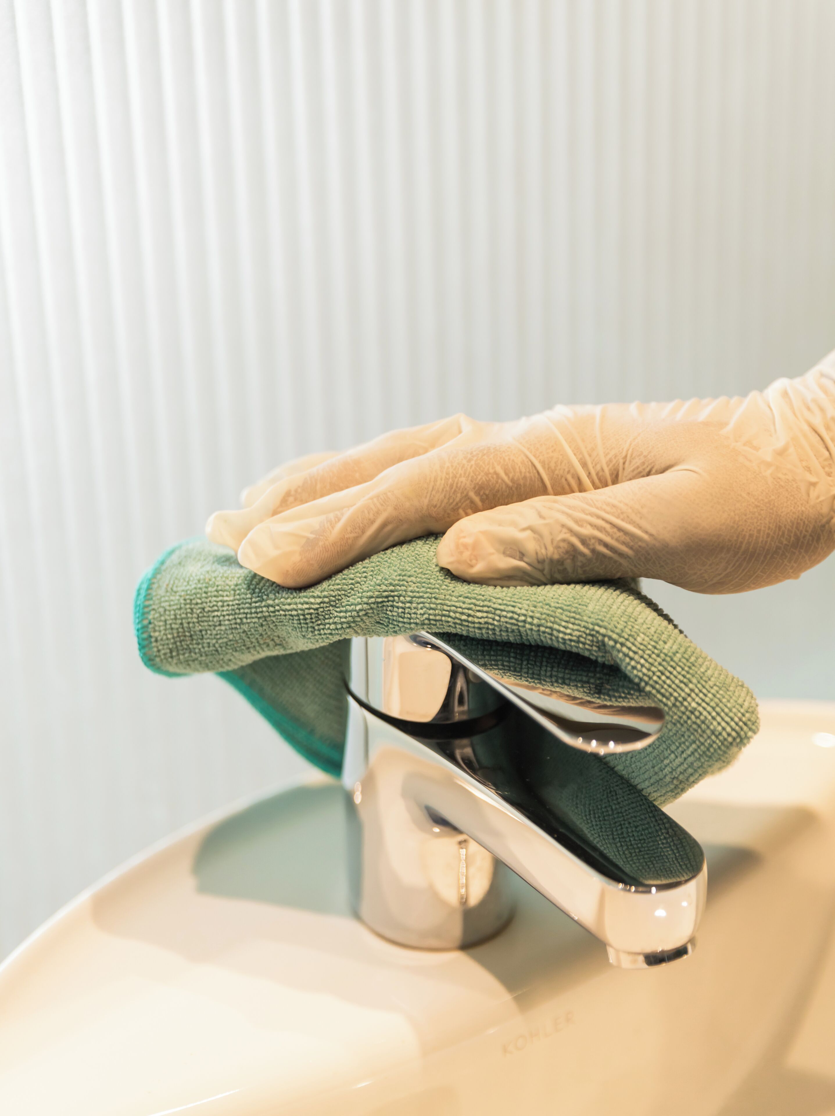 A hand cleaning a sink with a green cloth.