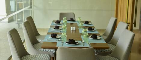 A dining area with a long table set for six, surrounded by six chairs with patterned cushions.