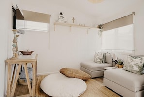 Een gezellige woonkamer met een beige bank, een klein houten tafeltje en een rond wit voetenbankje.