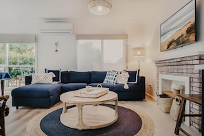 Een moderne woonkamer met een donkerblauwe hoekbank, een ronde houten salontafel en een open haard.