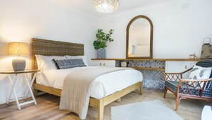 Un dormitorio con cama, mesita de noche, lámpara, espejo y silla de mimbre.