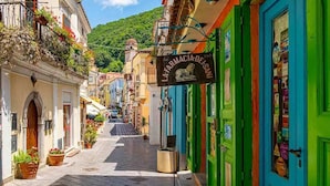 Una calle estrecha con edificios coloridos, un letrero de farmacia y macetas con plantas a lo largo de la acera.