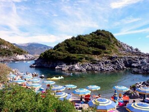 A coastal area with rocky terrain, a clear sky, and numerous beach umbrellas. - Villa Novella (Acquafredda)