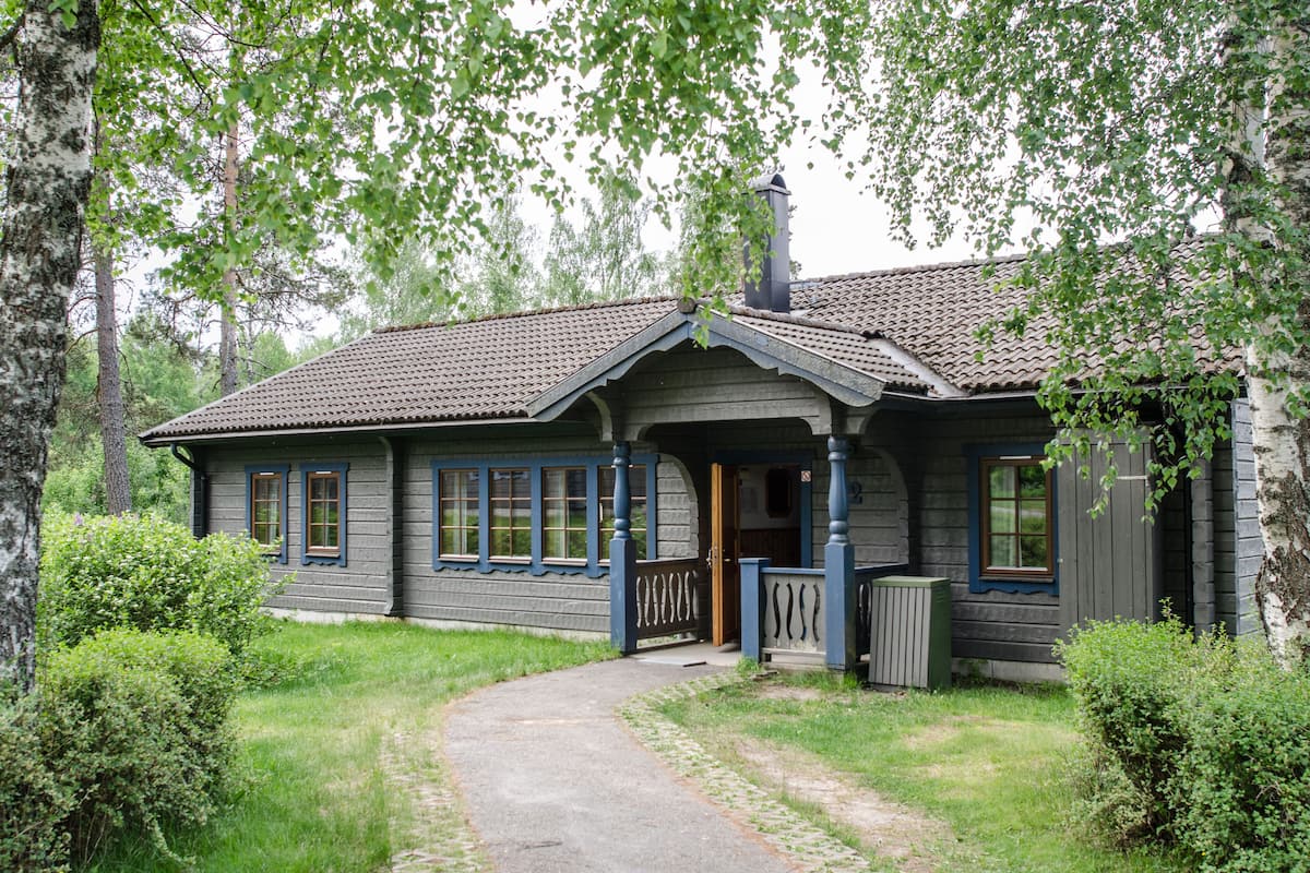 A rustic log cabin with a porch, a chimney, and a pathway leading to the entrance.