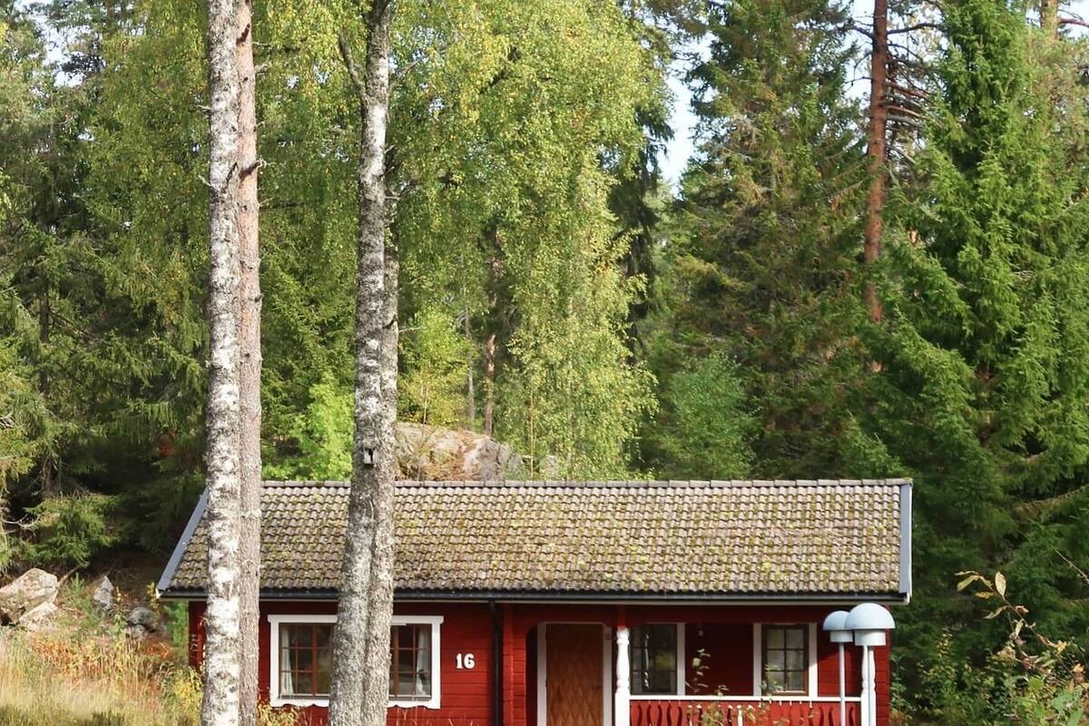A red cabin with a tiled roof, surrounded by trees and a stone wall.