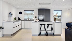 Een moderne keuken met een centraal eiland, barstoelen, een koffieapparaat en uitzicht op buiten.