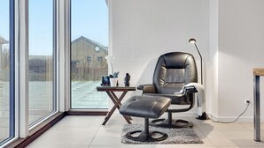 Een moderne kamer met een groot raam, een lederen fauteuil, een klein tafeltje en een vloerlamp.