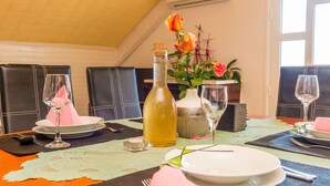 Une table à manger dressée avec des assiettes, des couverts et une bouteille de boisson, avec un vase de fleurs et une maquette de bateau en arrière-plan.