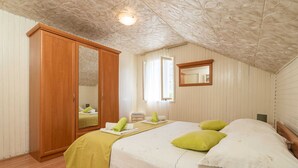 Une chambre avec une armoire en bois, un lit avec des coussins verts, une table de chevet et un miroir au mur.