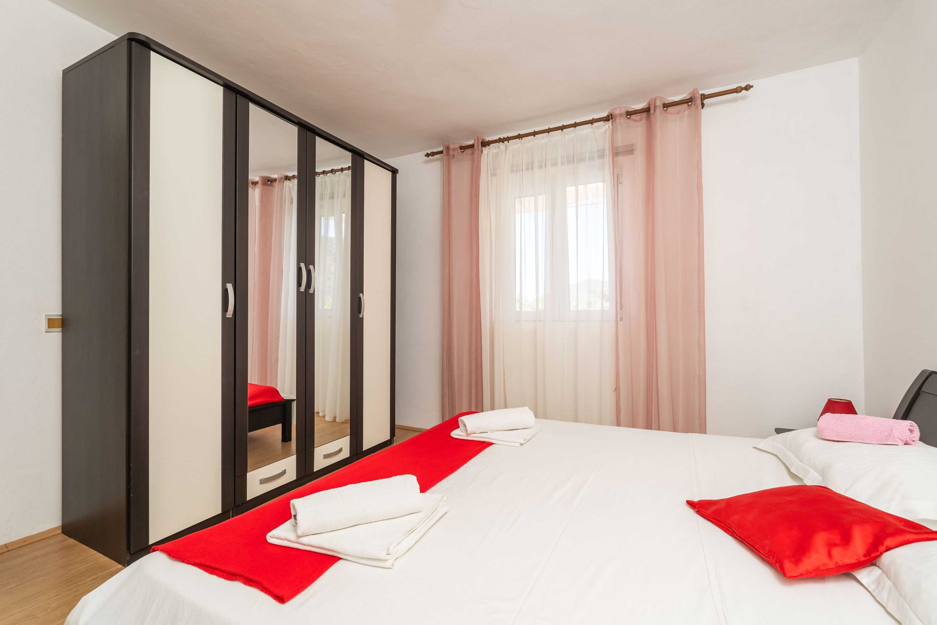 Une chambre à coucher avec un lit, une armoire, un miroir et une fenêtre avec des rideaux.