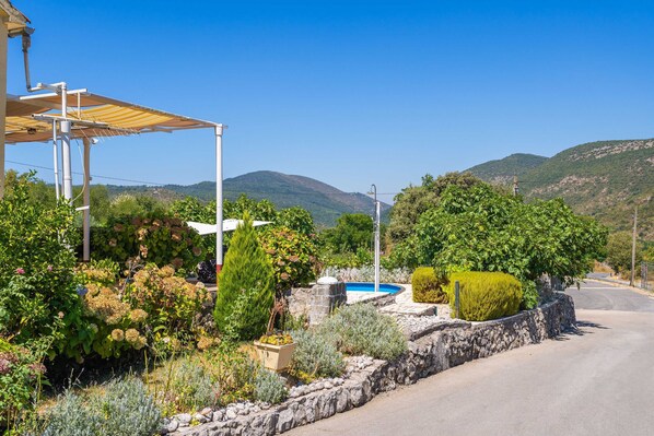 A rural road with a stone wall, a blue pool, and lush greenery.