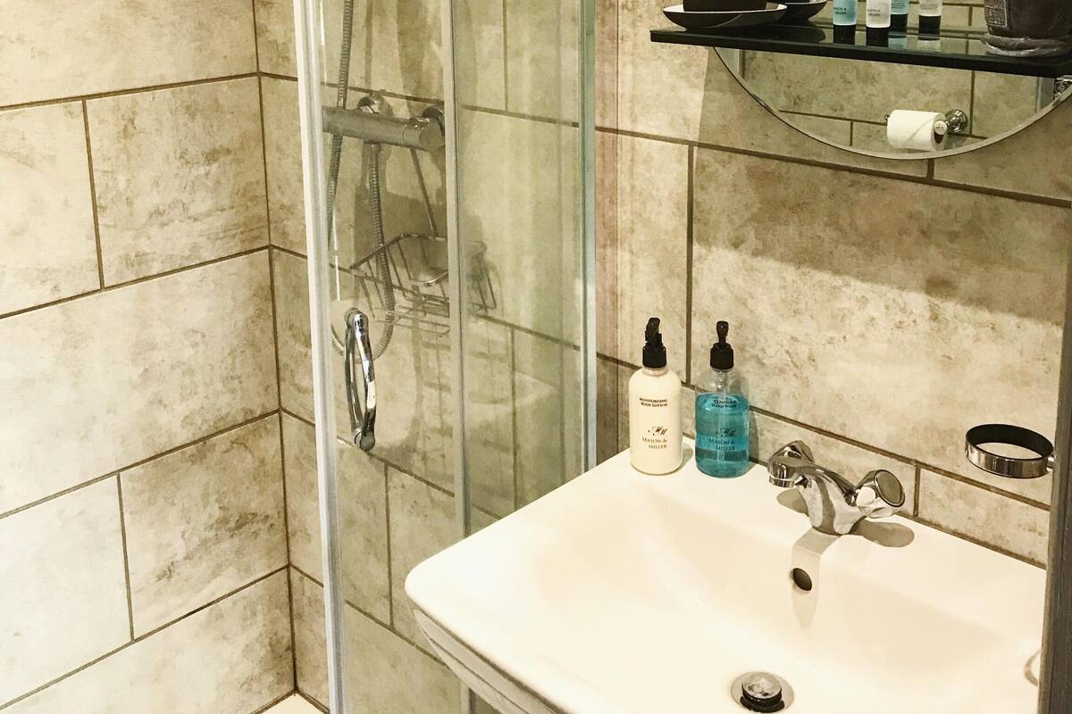 A bathroom with a glass-enclosed shower, a sink with a mirror above it, and toiletries on the sink.