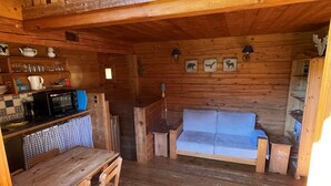 A rustic cabin interior with a wooden dining table, chairs, a sofa, a kitchenette with a microwave, and a loft area with a wooden railing. - old ,small ,typical chalet in the center of a mountain village :Le Grand Bornand (Le Grand Bornand)