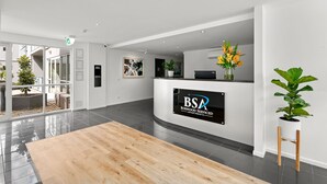 A reception area with a reception desk, a large wooden reception desk, a potted plant, and a view of the outside. - Modern and Spacious Two Bedroom Apartment (Burwood)