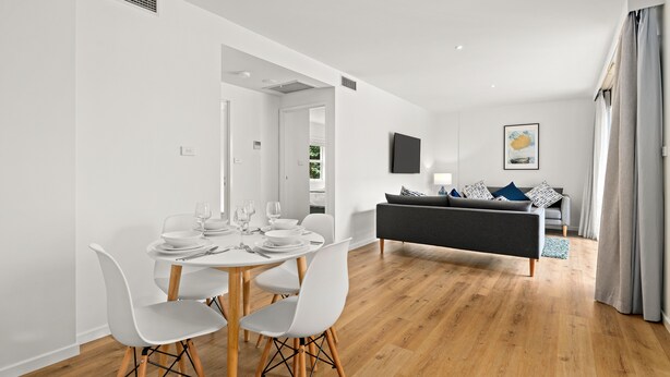 A modern living room with a sofa and a dining area with a table and chairs. - Modern and Spacious Two Bedroom Apartment (Burwood)