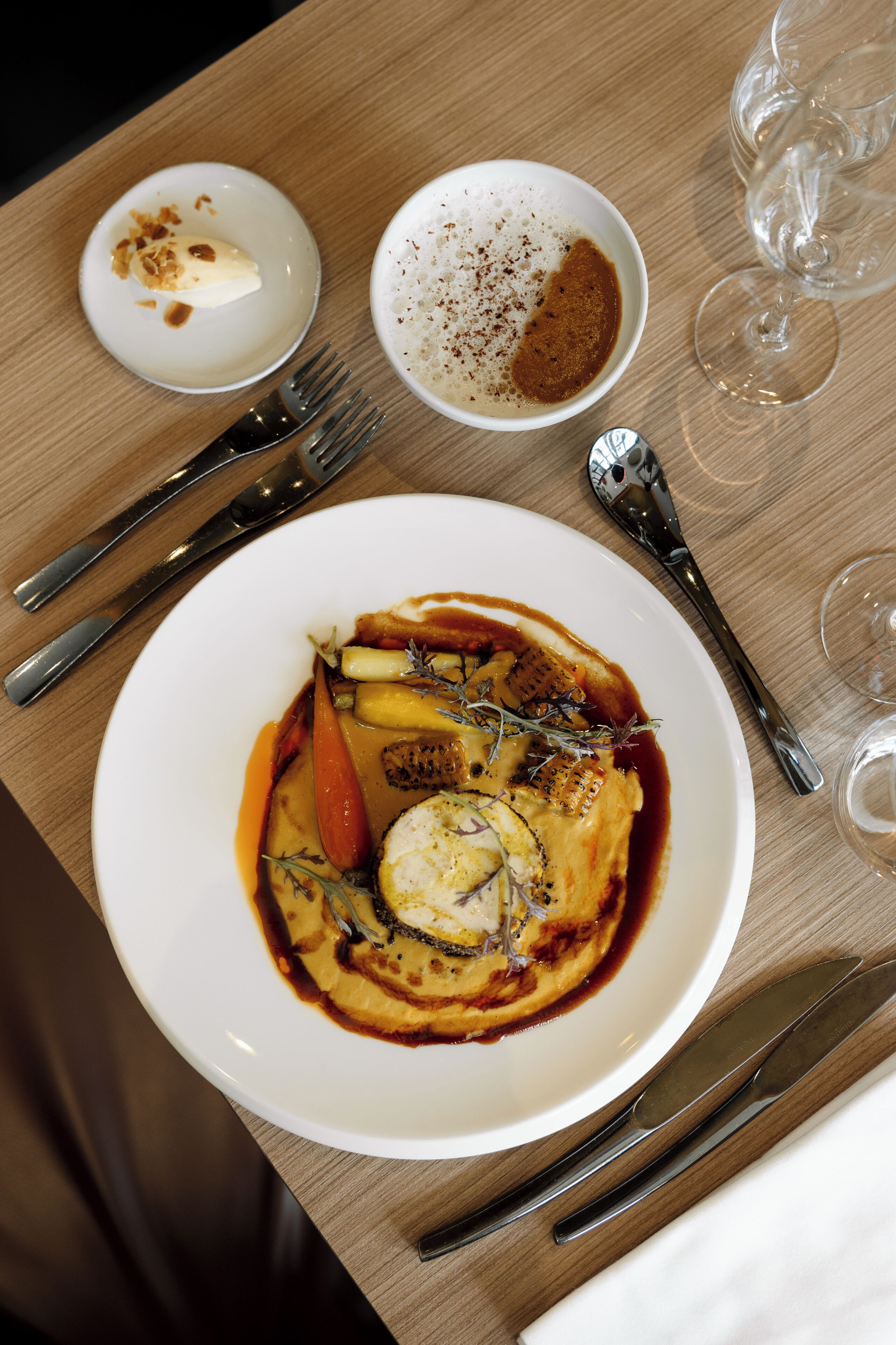 A dining table with a plate of food, a bowl of sauce, and a spoon.