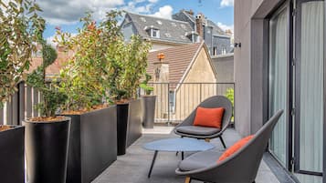 A balcony with a modern chair, a small table, and large black planters with plants.