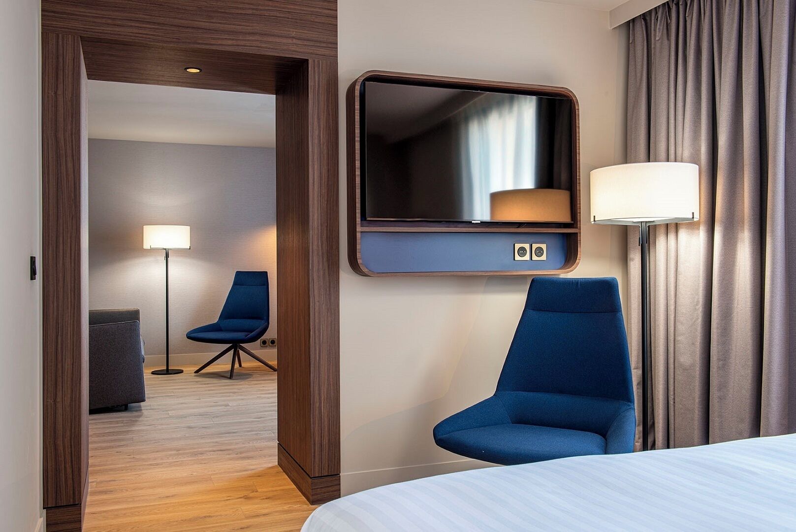 A hotel room with a bed, a desk, a chair, a mirror, and a lamp.