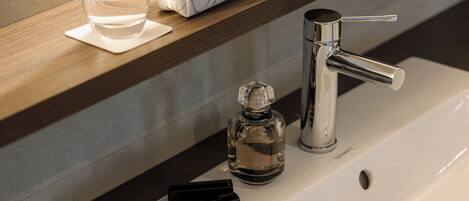 A bathroom with a white sink, a mirror, a bottle of hand soap, a glass of water, a makeup kit, and a towel.