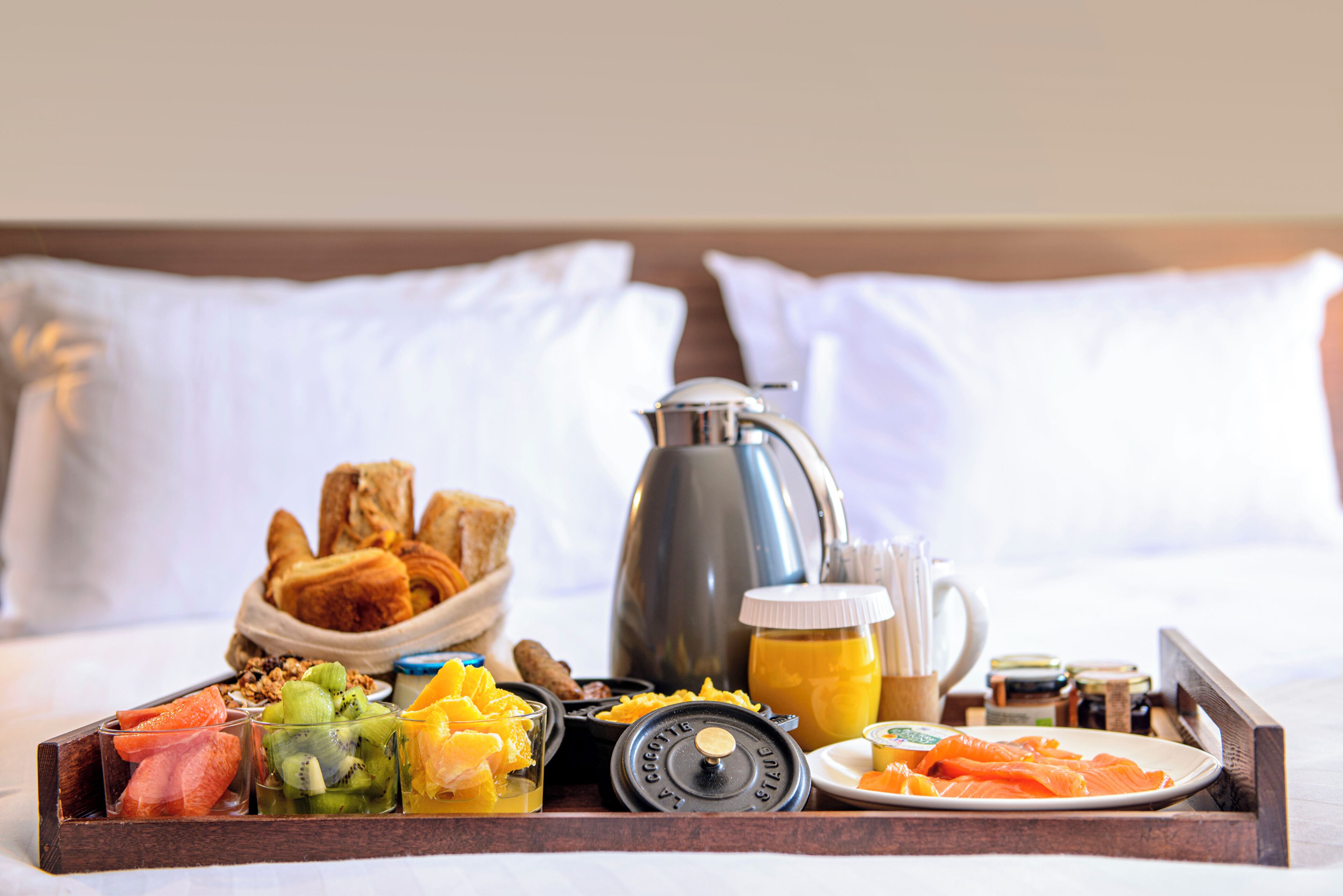 A breakfast tray with pastries, fruits, and beverages on a bed with white pillows.