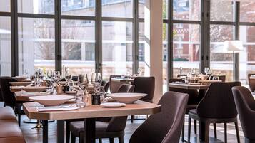 Un restaurant doté de nombreuses tables, de chaises et de verres à vin, avec de grandes fenêtres offrant une vue sur l’extérieur.