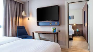 Ein Hotelzimmer mit einem Bett, einem Schreibtisch, einem Sessel, einem Fernseher und einer Tür zu einem weiteren Raum.