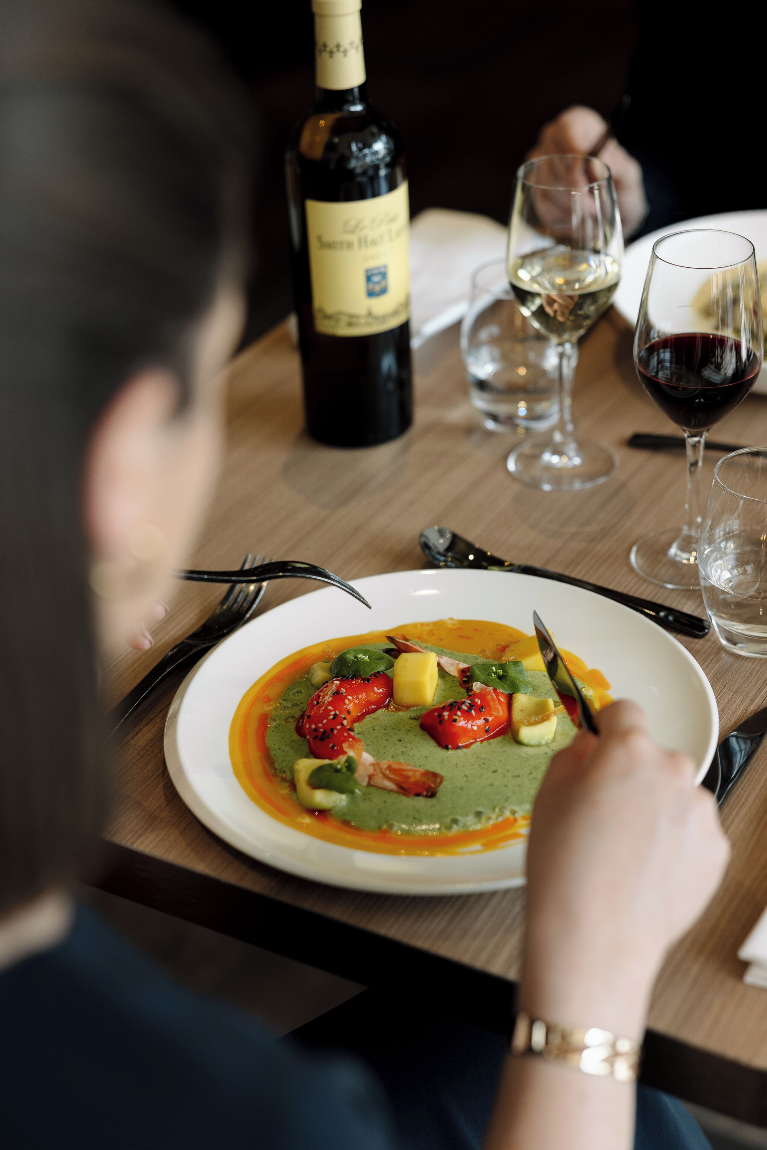 Una mesa de comedor con un plato de comida, una botella de vino y copas.