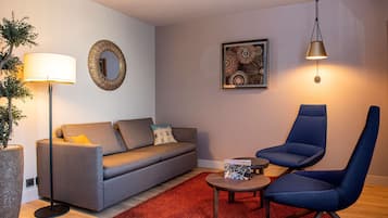 A modern living room with a grey sofa, a blue armchair, a red rug, a floor lamp, and a wall-mounted mirror.