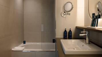 A modern bathroom with a glass-enclosed bathtub, a sink with a mirror, and toiletries on the countertop.