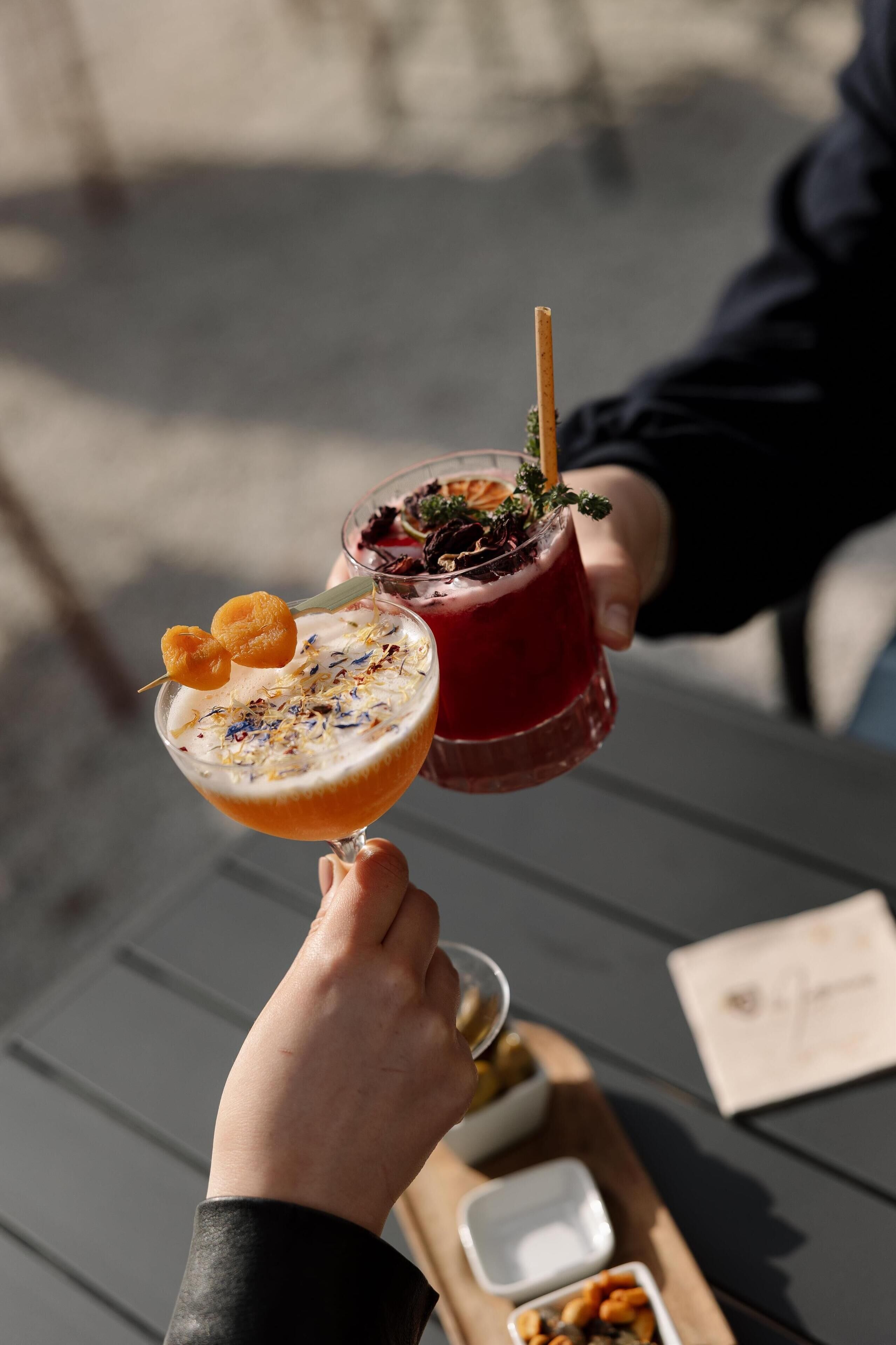 Une personne tient deux boissons dans ses mains, et sur une table, on aperçoit un plateau contenant de petites assiettes de nourriture et un menu.