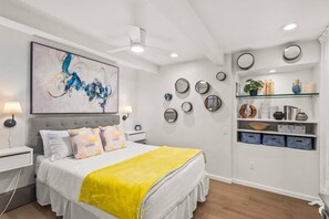 A modern bedroom with a large bed, a ceiling fan, wall-mounted mirrors, and a shelf with decorative items.