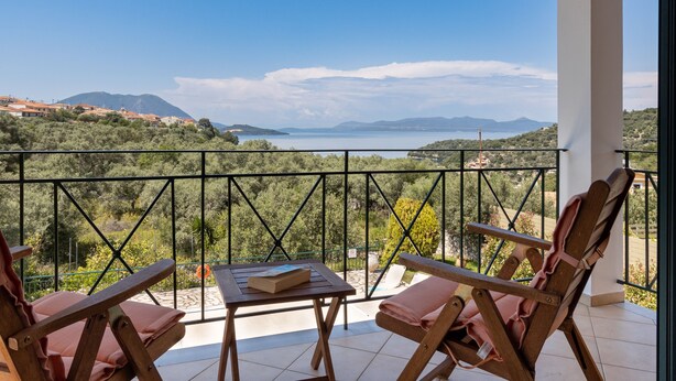 Un balcón con mesa y dos sillas, con vistas a un paisaje costero con montañas y una masa de agua.