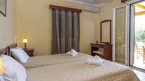 Habitación de hotel con dos camas, una mesita de noche con lámpara, baño con espejo y puerta corrediza de vidrio al exterior.