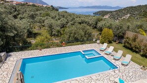 Una piscina con losetas de piedra, rodeada de vegetación y con vistas a un paisaje pintoresco con montañas y una masa de agua.
