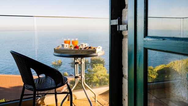 A balcony with a table set for breakfast, overlooking a body of water. - Potamitis Windmills & Apartments (Zakynthos)
