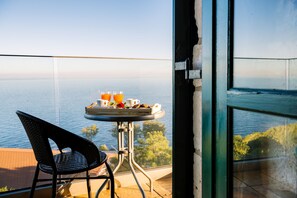 A balcony with a table set for breakfast, overlooking a body of water. - Potamitis Windmills & Apartments (Zakynthos)