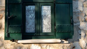 A stone wall with a green door featuring a decorative glass panel and a lantern above it. - Potamitis Windmills & Apartments (Zakynthos)