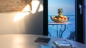 A table with a fruit bowl and a white flower centerpiece, a painting of a windmill, and a view of the sea through an open door. - Potamitis Windmills & Apartments (Zakynthos)