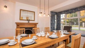 A dining room with a wooden table set for four, a fireplace, and a large window with curtains. - *Relocation, Business and Contractor Long Stays! (Oxford)