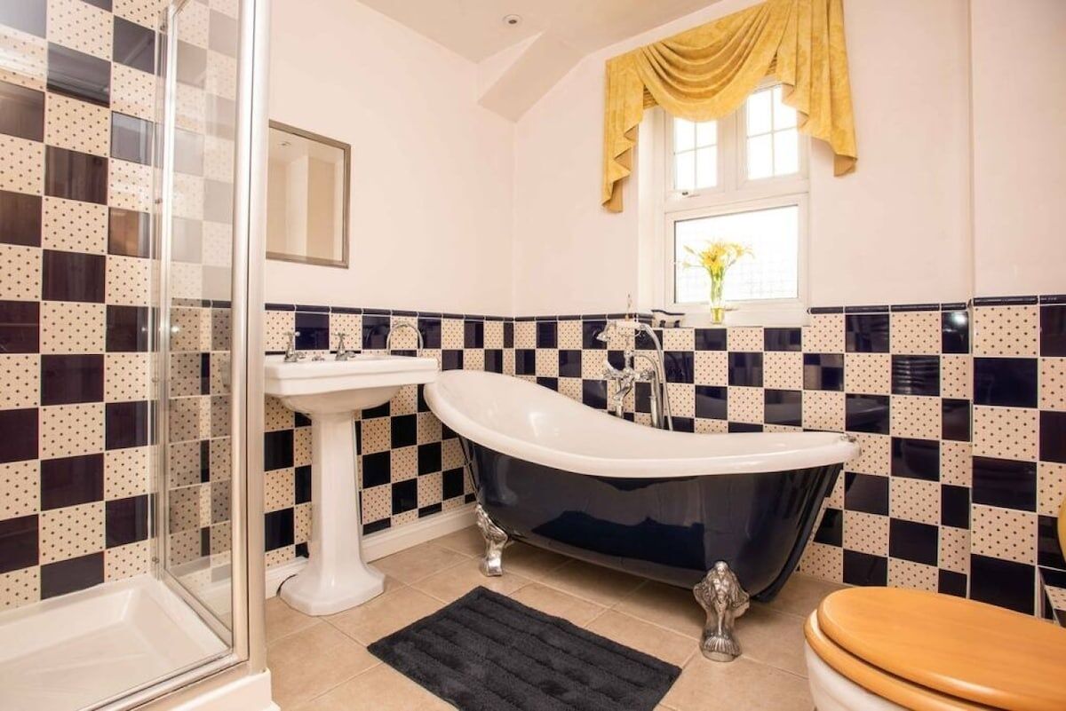 A bathroom with a checkered tile backsplash, a freestanding bathtub, a pedestal sink, and a glass shower enclosure.