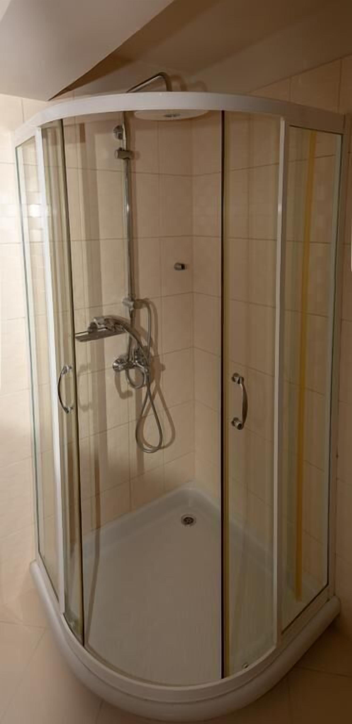 Ducha envuelta en vidrio con diseño curvo, cabezal de ducha de mano y panel de control.