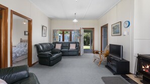 A spacious living room with a fireplace, a sofa, a TV, and a bed in the adjacent room. - Marina Views - Motuoapa Bach (Motuoapa)
