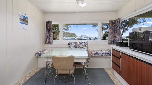 A compact kitchen with a dining area, a view of the marina, and a television on the counter. - Marina Views - Motuoapa Bach (Motuoapa)