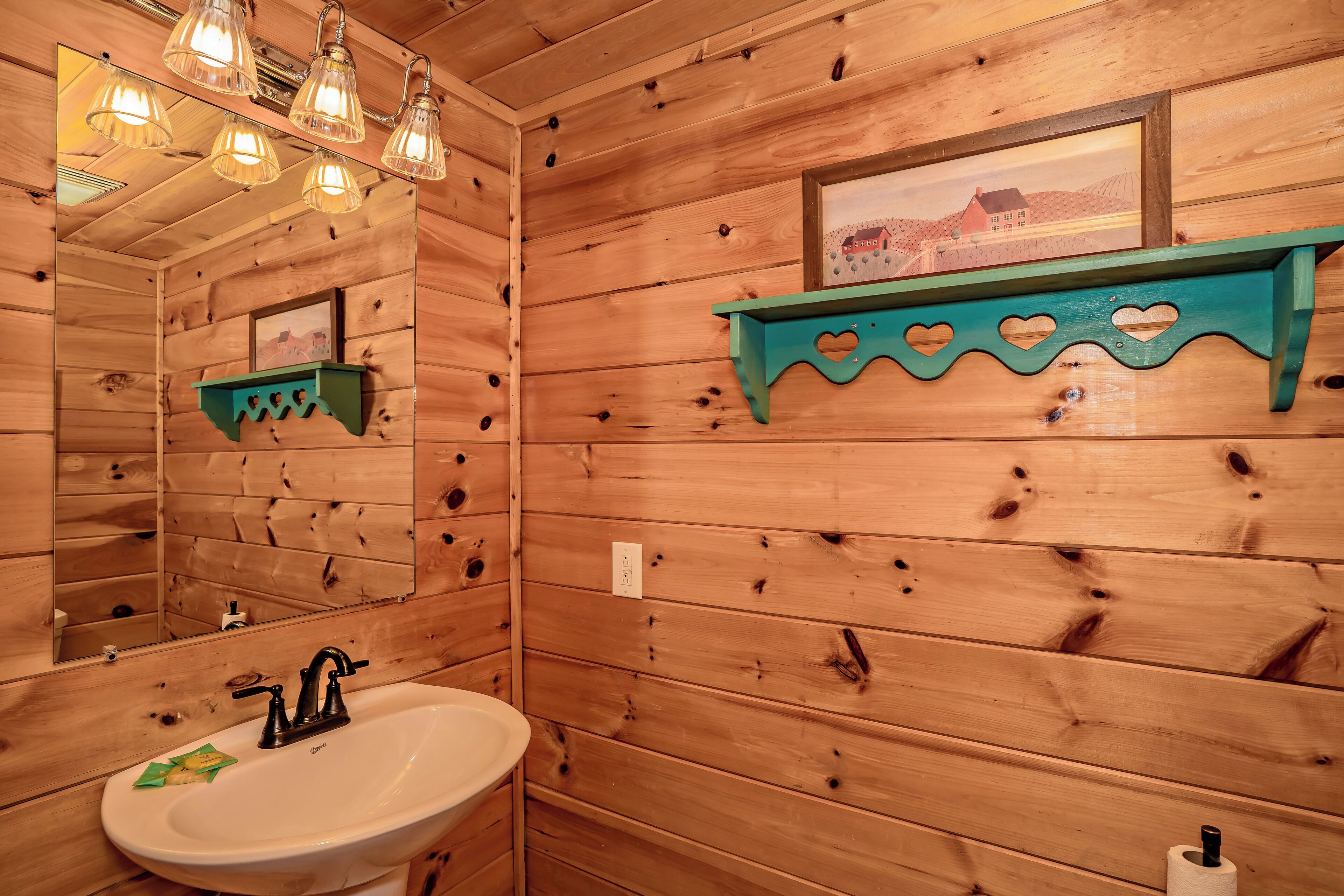 Une salle de bain rustique, avec des murs en bois, comprenant un lavabo, un miroir et des luminaires suspendus.
