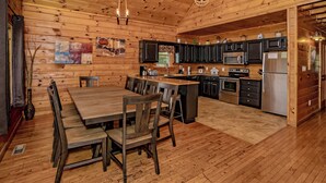 Interior de una cabaña de madera con comedor, cocina y un gran techo de madera.