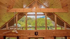 Una cabaña de madera con techo alto, ventilador de techo, decoración de cabeza de oso y vista a un área boscosa.
