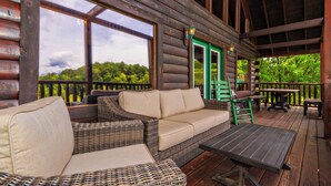 Una terraza de madera con mobiliario de mimbre, una mesa y vistas al bosque.
