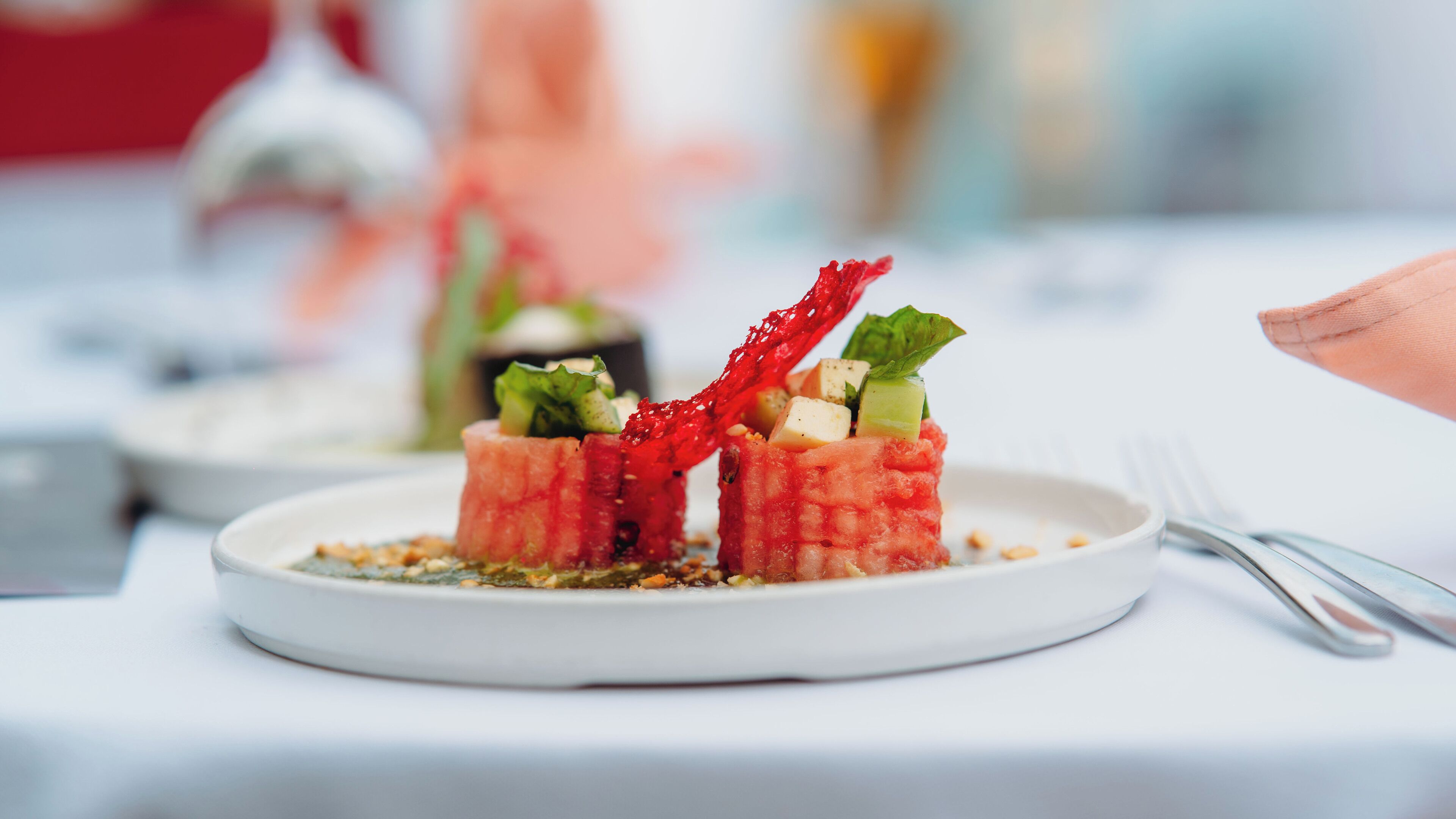 A plate of food with a red garnish and green leaves, on a white tablecloth.