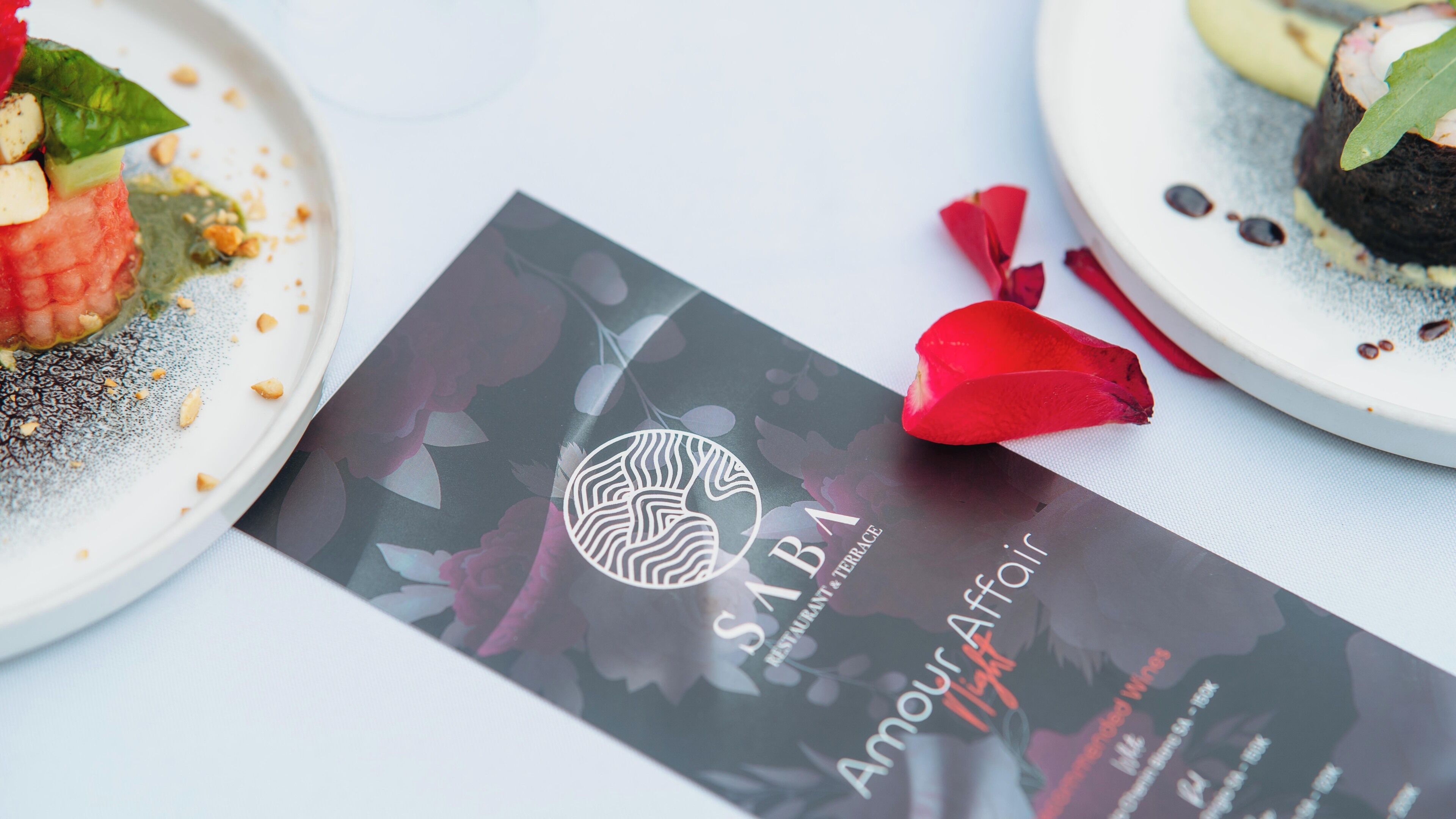 A brochure with the text "SAIBA Amour Affoire" and a logo, placed on a table with plates of food.