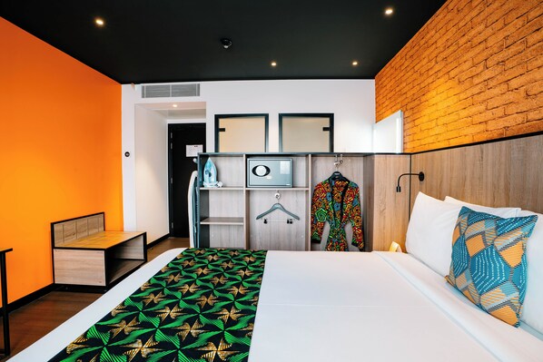 Una habitación de hotel moderna con una cama, un cabecero de madera, un armario y un perchero.